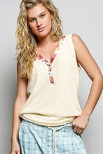 Cream-colored ribbed knit sleeveless top with contrast floral neckband and button details in v-neck design