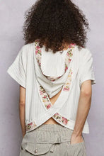 White floral-trimmed pol short sleeve hooded top with draped open-back design shown from the back side