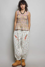 A woman wears a pol smocked printed square neck peplum tank with ruffle trim and matching embroidered carrot pants