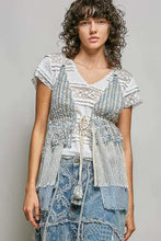 A layered distressed denim and lace top with a white v-neck base light blue frayed panels and subtle stripe center tie detail