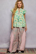 A woman wears a green and white floral print POL tassel tied floral flutter sleeve blouse with ruffled sleeves and embroidered hem
