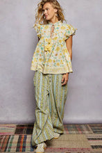 A woman wearing a light-colored pol tassel tied floral flutter sleeve blouse with yellow embroidery and ruffled sleeves