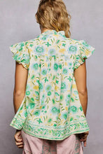 A woman wears a POL tassel tied floral flutter sleeve blouse with ruffled sleeves and hem in green and yellow tones