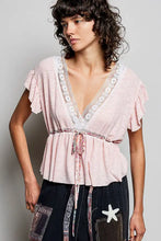 A soft pink short sleeve blouse with ruffles, lace-trimmed v-neck, and tied waistband for elegant wear