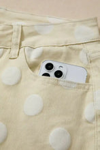 White iphone with triple-camera system peeking from beige polka dot pattern denim pocket of polka dot wide leg jeans