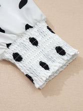 White blouse with black polka dots featuring smocked cuffs in a stylish polka dot long sleeve design