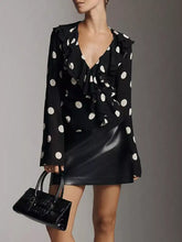 Black polka dot ruffle v neck blouse featuring ruffled sleeves and neckline in lightweight fabric for stylish wear