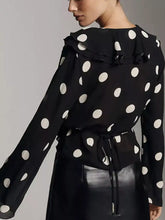 Black polka dot ruffle v neck blouse with white circular patterns, long sleeves, and a ruffled neckline