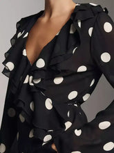 Polka dot ruffle v-neck blouse featuring black fabric with white circular patterns and layered ruffled sleeves