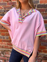 Pink ribbed knit short-sleeved top with rainbow trim collar and cuffs featuring side slits in a ribbed knit polo style