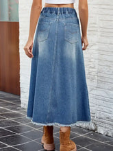 Raw hem blue denim skirt with waist stretch elastic waistband and buttoned front pockets in maxi length