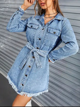 Light-wash denim dress with raw hem collared neck, long sleeves, frayed cuffs, and belted waist button front closure