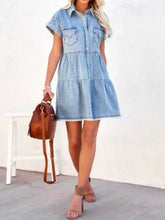 A light-wash denim dress with short sleeves, button front, chest pockets, and a raw hem short style