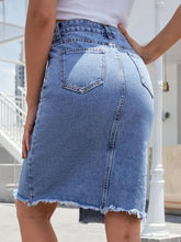 A light blue wash denim skirt with raw hem slit, mid-thigh length, frayed hem, and back pockets