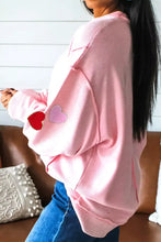 Pink ribbed chenille long sleeve top with glitter trim and red and light pink heart patches on the sleeve