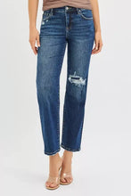 Dark-wash denim jeans with a distressed tear at the knee and frayed edges, featuring a classic five-pocket design.