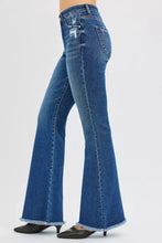Back view of blue denim risen high rise flare jeans featuring a distressed patch on the pocket and frayed hems