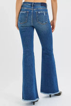 Back view of risen high rise flare jeans in blue denim featuring frayed hems and distressed back pockets