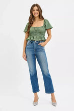 A woman wearing risen tummy control high rise crop straight blue denim jeans paired with a green ruched top