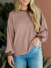Woman in round neck drop shoulder long sleeve sweatshirt with mauve ribbed balloon sleeves and light wash jeans