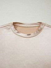A blush-pink round neck tank top with satin trim and smooth textured fabric featuring a gold metallic detail