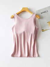 A soft pink round neck tank with a smooth shiny fabric hangs neatly on a wooden hanger