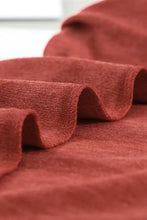 A soft rust-colored round neck top with textured weave and ruffled folds showcasing long sleeve length