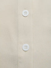 White plastic buttons with four holes on a beige fabric detail of a ruffle sleeve tie-neck shirt