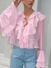 A delicate pink ruffle trimmed long sleeve blouse with bell sleeves and a layered flowing design