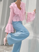 A delicate pink ruffle trimmed long sleeve blouse with flared sleeves and v neckline crafted from lightweight sheer fabric