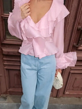 A soft pink ruffle trimmed long sleeve blouse with voluminous sleeves and a deep v-neckline