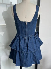 Back view of a blue denim dress with a corset-style back, central zipper, and layered ruffles on the hem