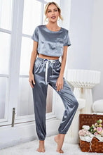 Gray satin pajama set with short sleeve cropped top featuring a front pocket and matching drawstring pants