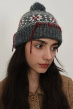 Gray geometric knit hat with pom-pom, snowflakes, and red seam trim