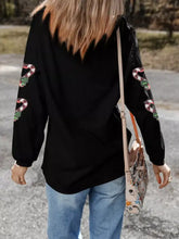 Black ribbed long-sleeve top with embroidered red white and green snakes on sleeves for candy cane heart care instructions