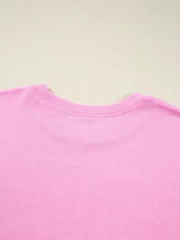 A soft pink cotton crewneck t-shirt with a ribbed neckline featuring a slightly stretchy sequin xoxo exposed seam design