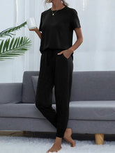 Black short-sleeved top with elastic waistband and side pockets featuring a shiny round neck and comfortable sleeve length
