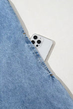 A sleek white iphone peeking from the pocket of a blue denim mini dress with short sleeves and a collared patch pocket