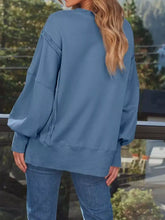 A soft dusty blue oversized sweatshirt with side slit, ribbed cuffs, relaxed fit, and care instructions tumble dry low