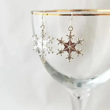 Two silver snowflakes earrings hanging from a glass