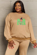 Plus-size woman in tan long-sleeved drop shoulder graphic sweatshirt with green Monster print