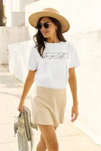 Woman in Simply Love letter graphic short sleeve t-shirt, beige skirt, straw hat