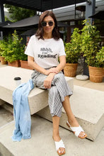 Woman in Simply Love SHHH Im Reading short sleeve t-shirt, striped culottes, white sandals