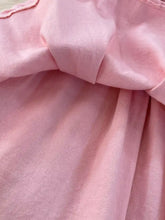 A soft pink sleeveless belted denim dress with textured fabric and a gathered waistband