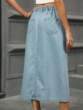 Back view of light-wash denim midi skirt with elastic waistband and two back pockets slit button detail denim midi skirt