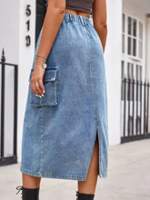 Slit buttoned denim skirt featuring mid-thigh length, elastic waistband, large side pocket, and front slit in blue denim