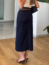 Dark blue denim skirt with straight cut and visible stitching details featuring a front slit and tumble dry care instructions