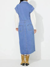 Back view of blue denim dress with slit half button collared neck cap sleeve and two back pockets worn over white shirt