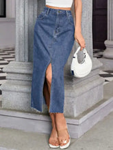 A medium blue midi denim skirt with front slit, frayed hem, and pockets in mid-thigh length design