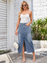 A white crossbody handbag with structured flap and gold-tone hardware paired with a slit midi denim skirt with pockets and waist stretch